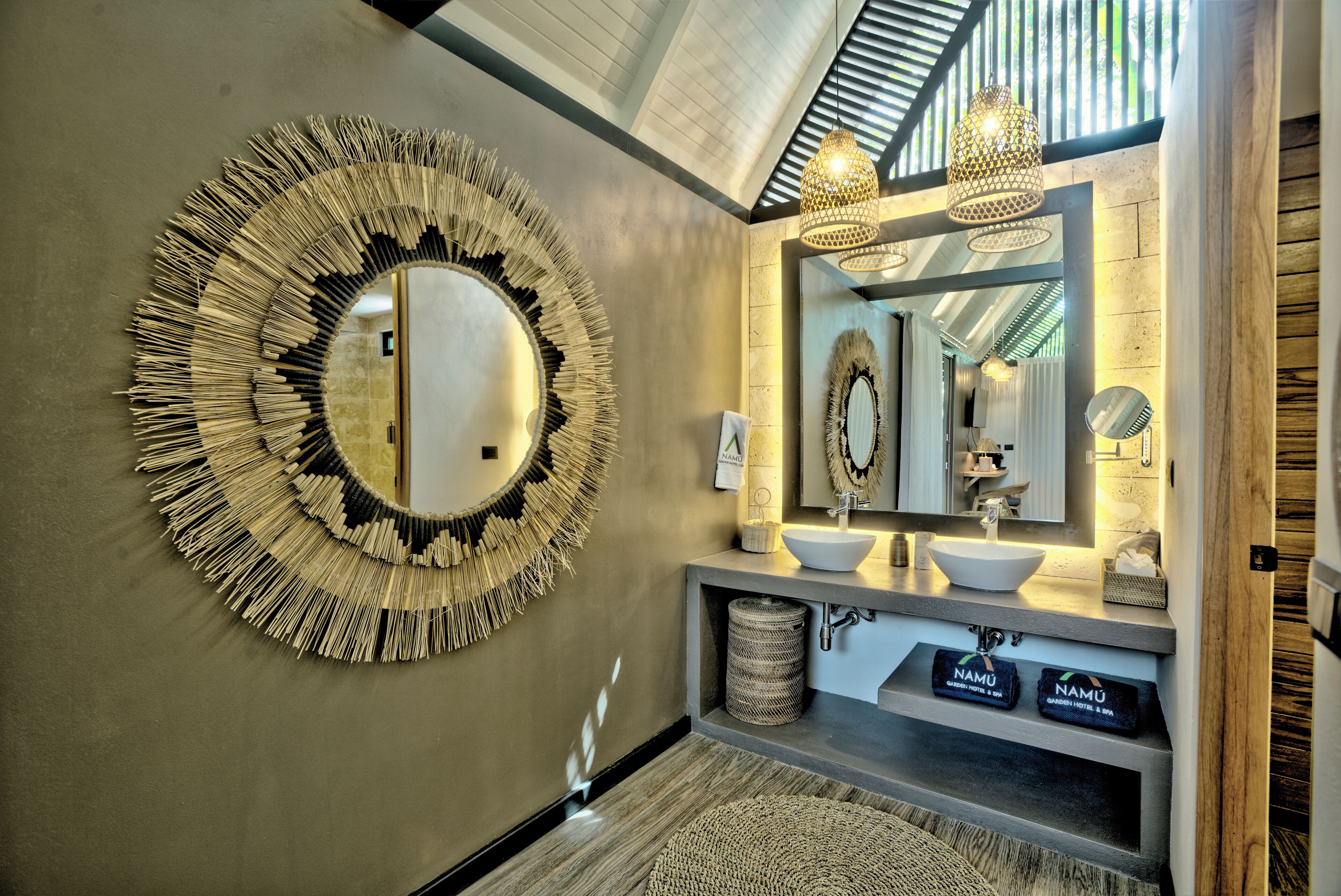 Un baño moderno con un espejo circular grande, dos lavamanos y techo de madera.