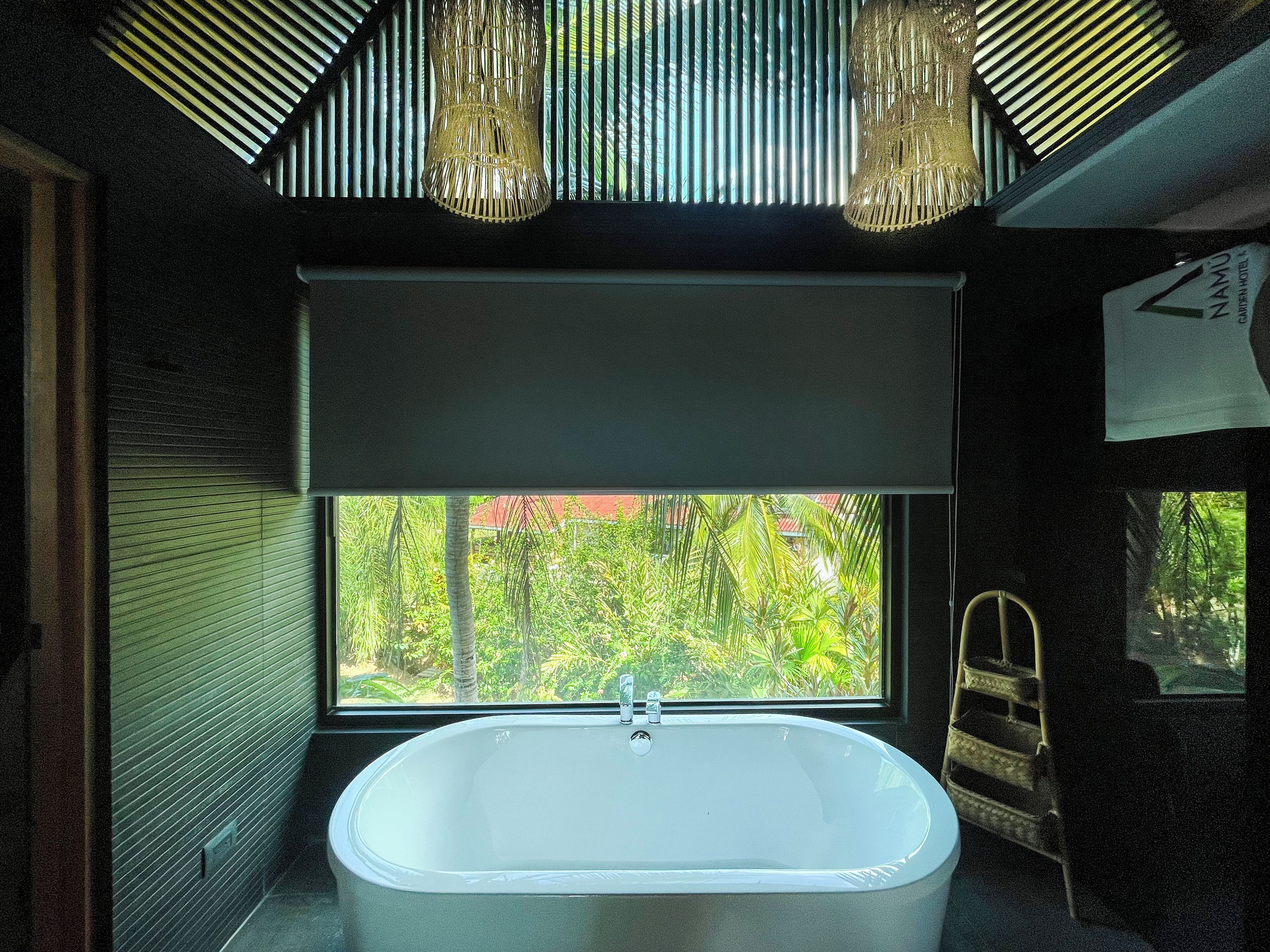 A modern bathroom with a freestanding bathtub, a large window with a view of greenery, and a ceiling with a unique light fixture.
