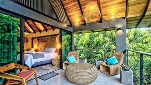 A modern bedroom with a glass wall, a large bed, and a balcony with wicker furniture and plants. - Namu Garden Hotel & Spa - Adults Only (Cahuita)