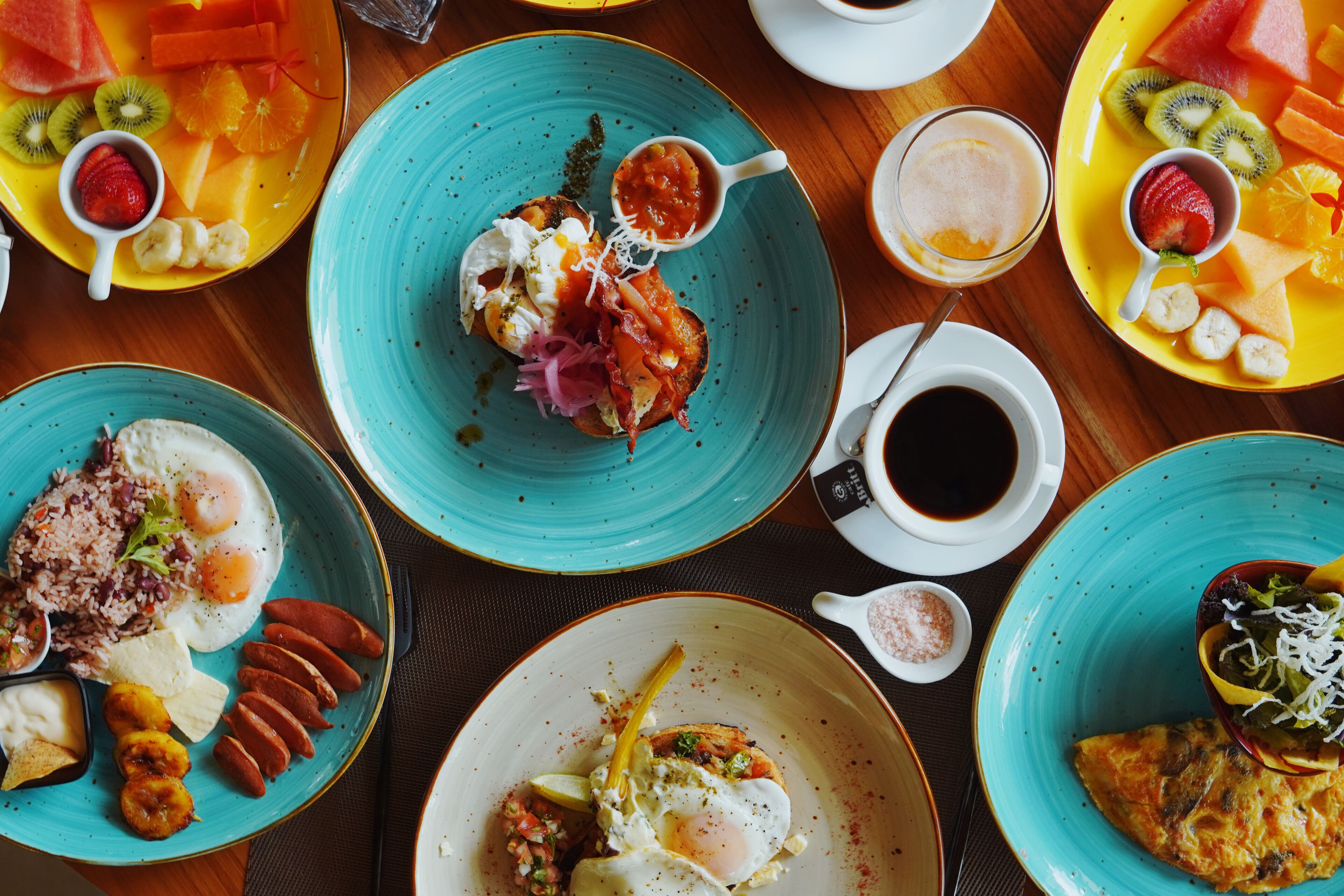 A variety of dishes on multiple plates, including fruits, vegetables, and eggs, suggesting a breakfast setting.