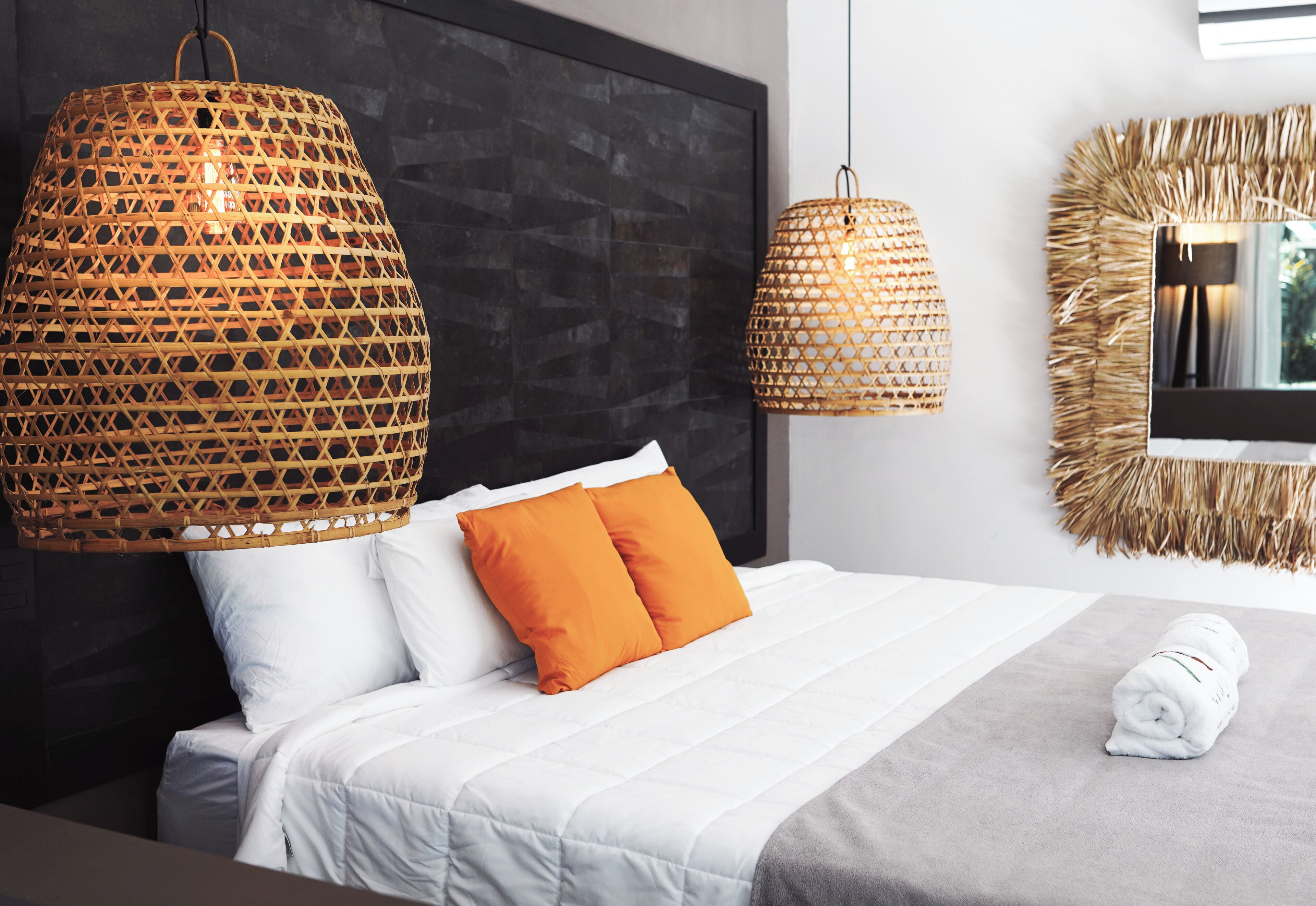 Une chambre d’hôtel moderne avec un grand lit, deux oreillers orange, une couverture blanche et deux lampes en osier.
