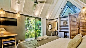 A spacious bedroom with a large bed, a desk, and a TV. There is a window with a view of greenery outside. - Namu Garden Hotel & Spa - Adults Only (Cahuita)