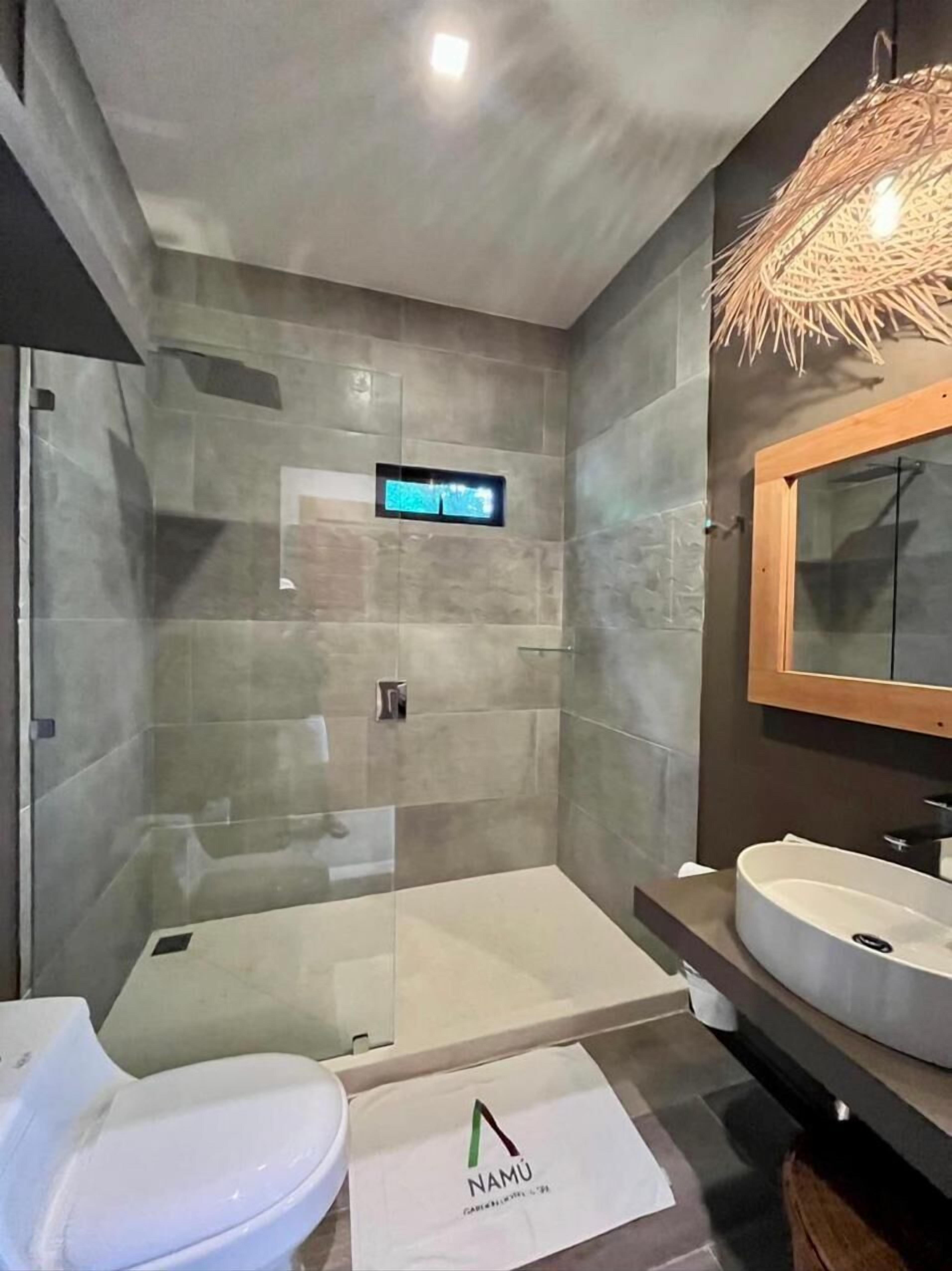 Une salle de bain moderne avec une douche à parois de verre, des toilettes blanches, un meuble-lavabo avec un miroir et un panneau numérique fixé au mur.