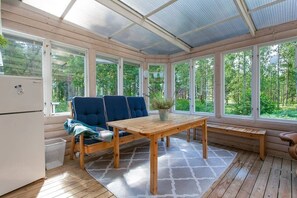 A sunroom with a wooden table and chairs, large windows, and a view of greenery.