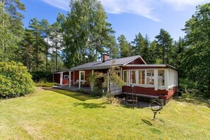 A red wooden house with a porch, surrounded by a well-maintained lawn and tall trees.