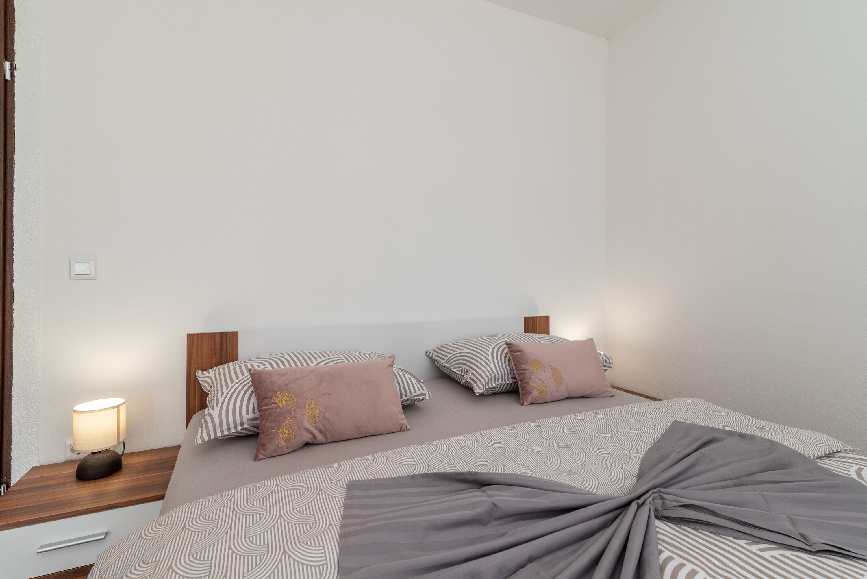 Un lit bien fait, avec une literie à motifs, une lampe de chevet et une tête de lit en bois.