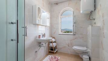 Un baño con ducha, inodoro, lavabo y una ventana con vistas.