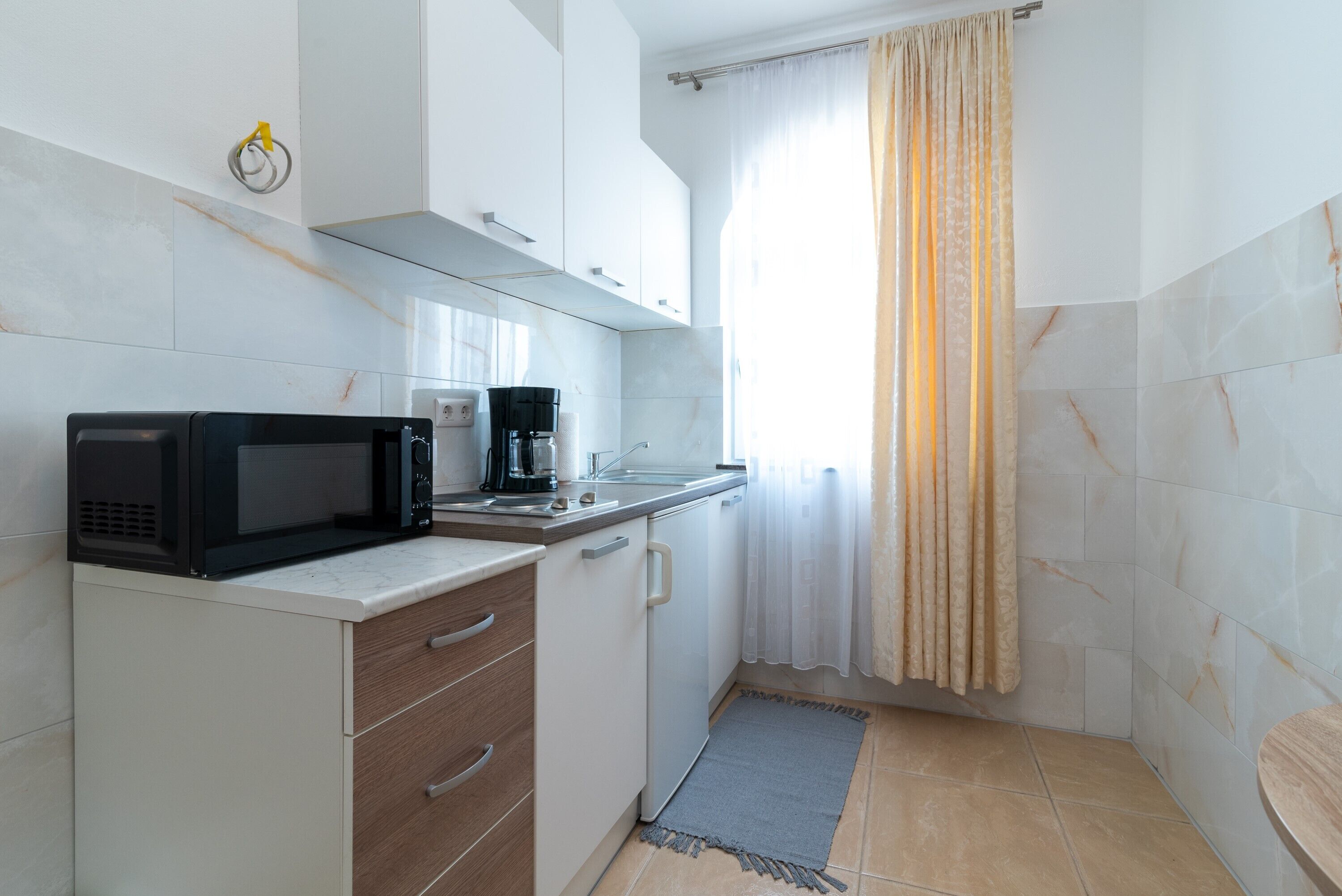 Cocina compacta con microondas, cafetera y un lavamanos pequeño.