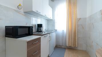 Cocina compacta con microondas, cafetera y un lavamanos pequeño.