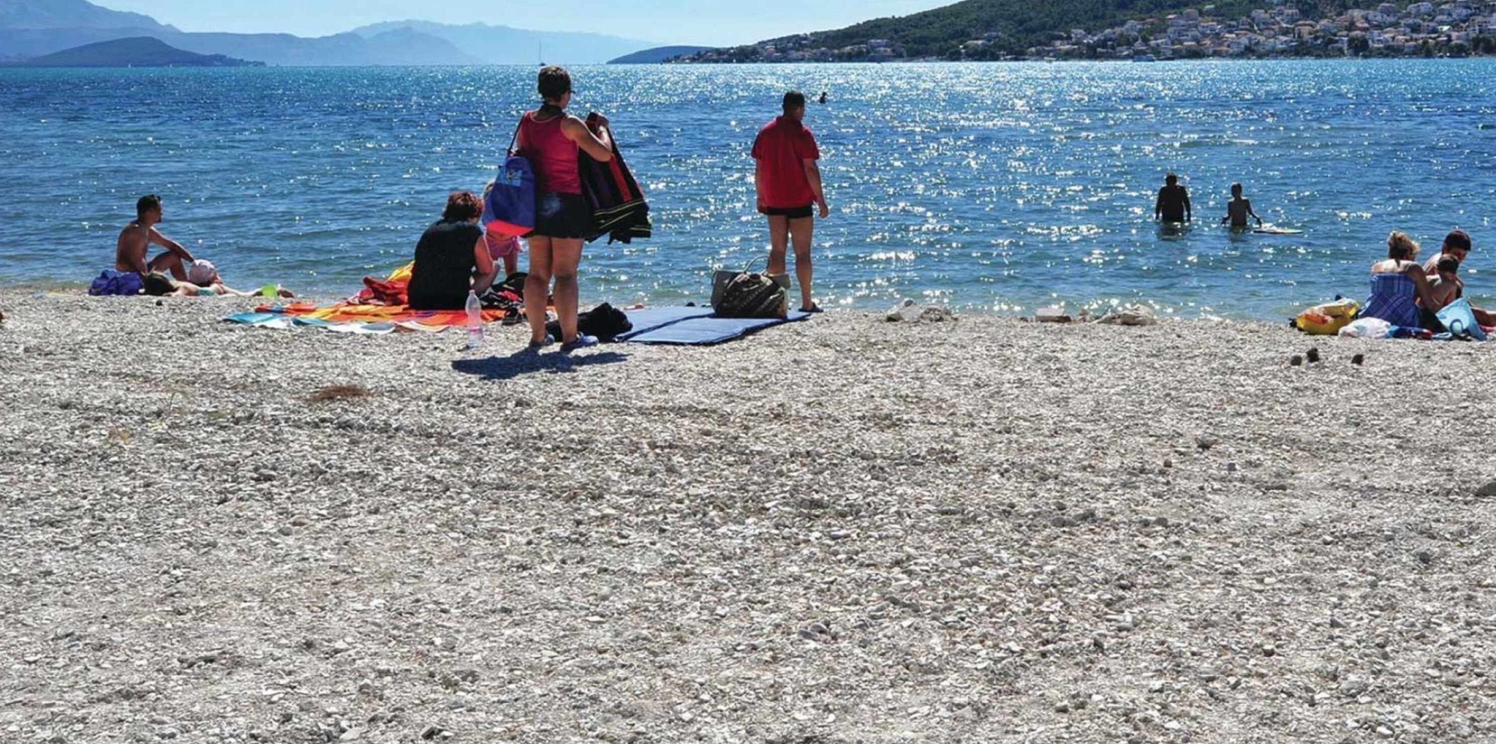 A pebbled beach with people sunbathing and swimming.