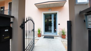 A building entrance with a black gate, a blue door, and two potted plants. - Appartamento La Rosa (Roe Volciano)