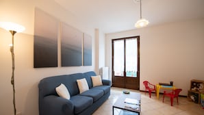 A living room with a blue sofa, a coffee table, a lamp, and a door leading to a balcony. - Appartamento La Rosa (Roe Volciano)