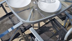 Ein Glastisch draußen mit weißen Tellern, Weingläsern und einer Champagnerflasche.