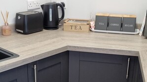 Eine moderne Küche mit dunklen Schränken, einem schwarzen Toaster, einem Wasserkocher und einer Holzkiste mit der Aufschrift 'TEA'.