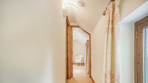 A narrow hallway with a wooden floor, a white chair in the distance, and a window with a wooden frame.