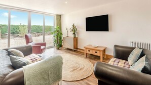 Un salon moderne avec des canapés en cuir, un tapis rond, une table basse en bois et un téléviseur fixé au mur.