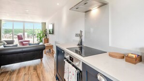 Une cuisine moderne dotée d’un four encastré, d’une hotte en acier inoxydable et d’une grande fenêtre donnant sur un jardin.