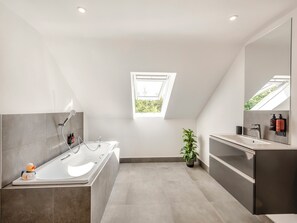 Un baño moderno con una bañera independiente, un espejo grande y un tragaluz.