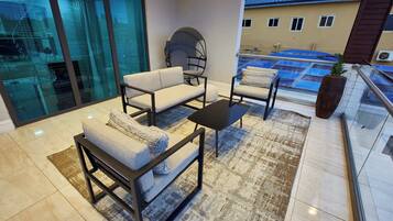 A modern living room with a sofa, armchair, and coffee table, a glass door leading to a balcony, and a view of a building across the street.