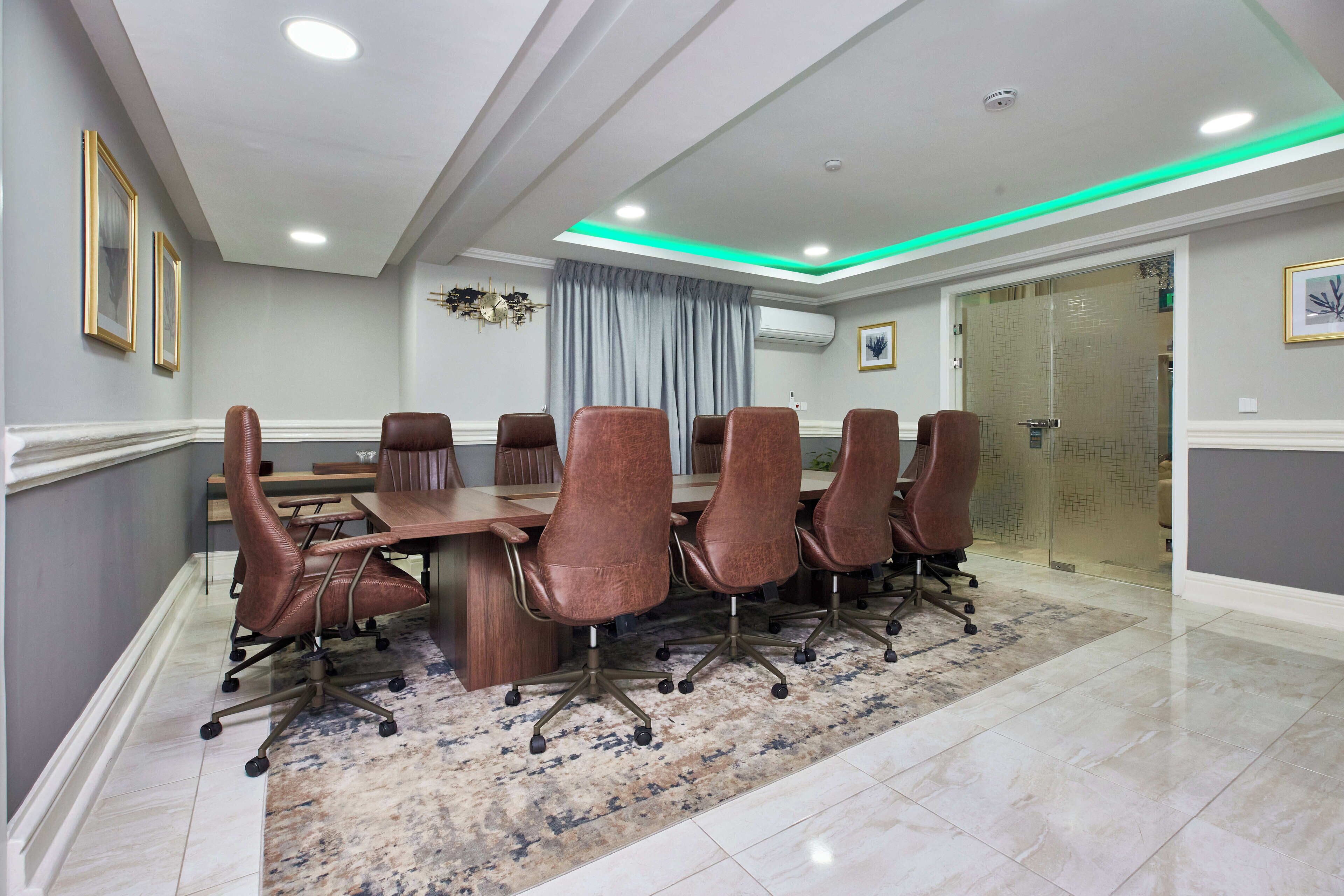 A conference room with a long table, six brown chairs, and a patterned rug.