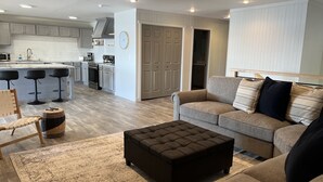 A modern living room with a grey sofa, a brown ottoman, and a patterned rug. - Driftwood House- Endless Ocean Views (Sitka)