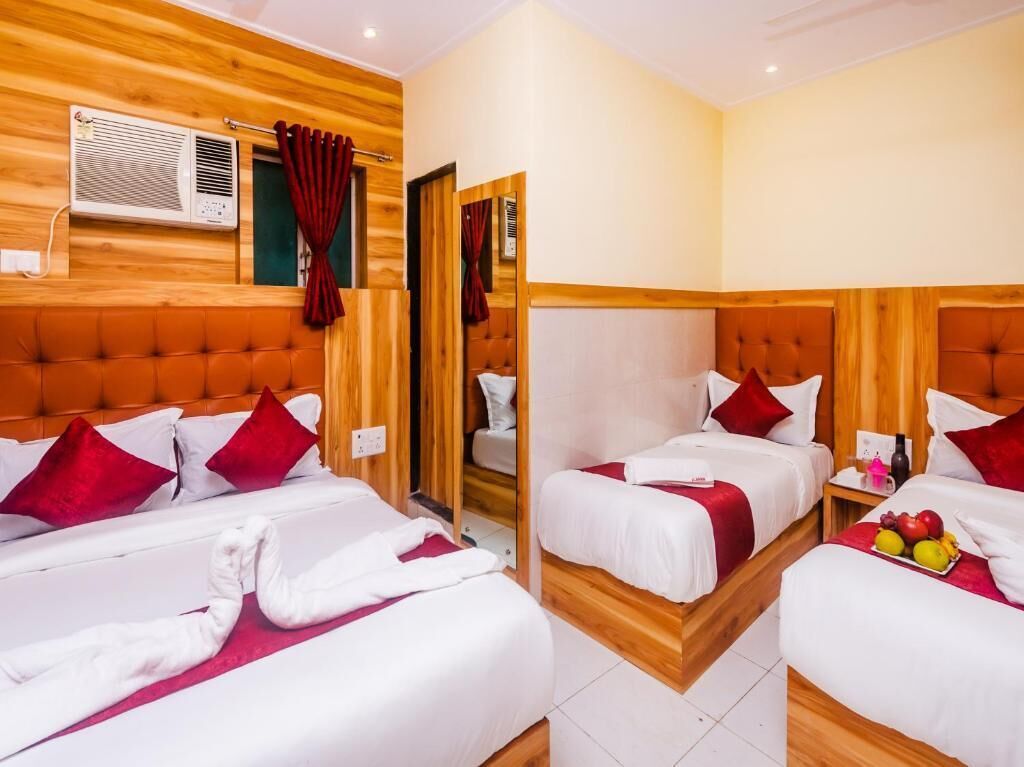 A hotel room with two beds, each with red and white bedding, and a wooden headboard. There is a small table with fruit and a bottle on it.