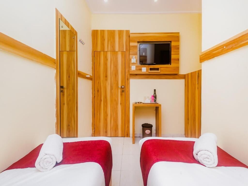 A hotel room with two beds, wooden paneling, a television, a small table with toiletries, and a trash bin.