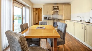 Eine moderne Küche mit einem Holztisch und -stühlen, einem eingebauten Backofen und Blick ins Freie durch eine Schiebetür.