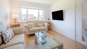 Ein Wohnzimmer mit einer Couch, einem Couchtisch, einer Lampe und einem an der Wand befestigten Fernseher.