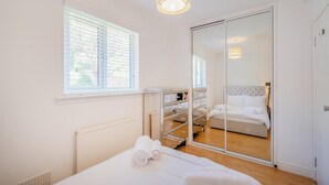 Ein Schlafzimmer mit einem Bett, einem großen Spiegel, einem Kleiderschrank und einem Fenster mit Jalousien.