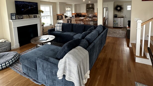 A spacious living room with a large sectional sofa, a fireplace, and a kitchen in the background. - Great home minutes from beautiful Moody Beach, for the perfect beach vacation! (Wells)