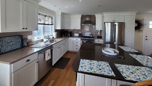 A modern kitchen with white cabinets, a stainless steel refrigerator, a gas stove, and a large island with star-patterned placemats. - Great home minutes from beautiful Moody Beach, for the perfect beach vacation! (Wells)