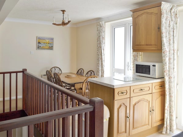 A kitchen with wooden cabinets, a dining table with chairs, a microwave, and a window with curtains.