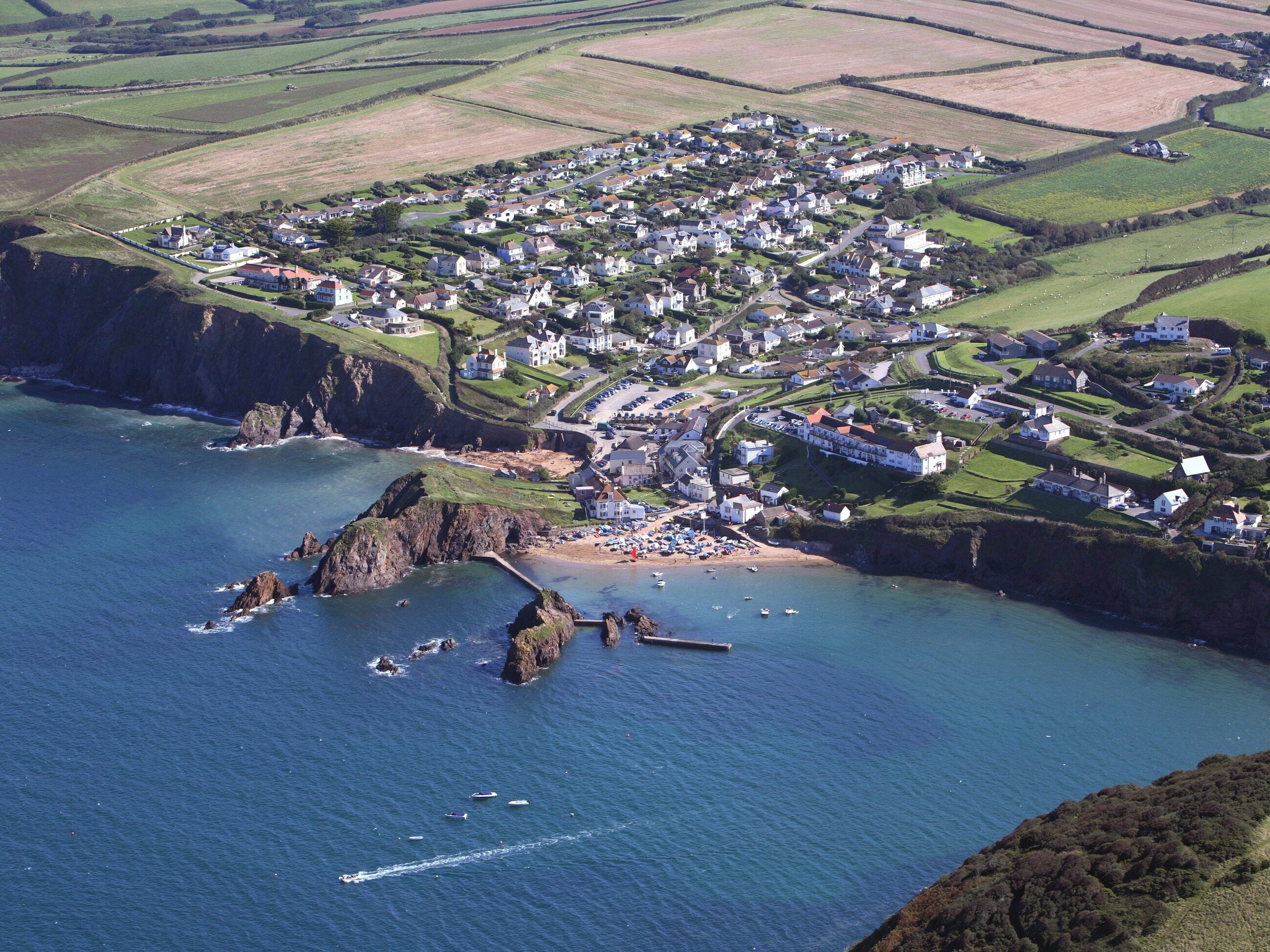An aerial view of a coastal village with houses, a beach, and rocky cliffs.