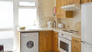 A compact kitchen with wooden cabinets, a built-in washing machine, a stove, and a refrigerator. - Smugglers Haunt - UK44513 (Hope Cove, near Kingsbridge)
