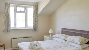 Une chambre à coucher comprenant un lit, une table de chevet, une lampe, une fenêtre avec des rideaux et un radiateur.