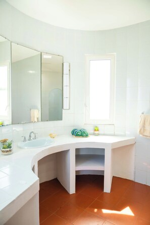 A modern bathroom with a white sink, a large mirror, and a window.