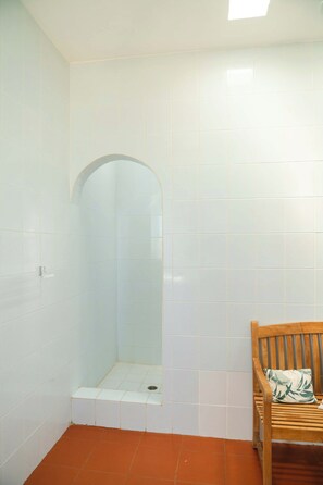 A bathroom with white tiled walls, a wooden bench, and a shower area.
