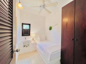 A small, clean room with a bed, a bedside table with a lamp, a window, and a ceiling fan.