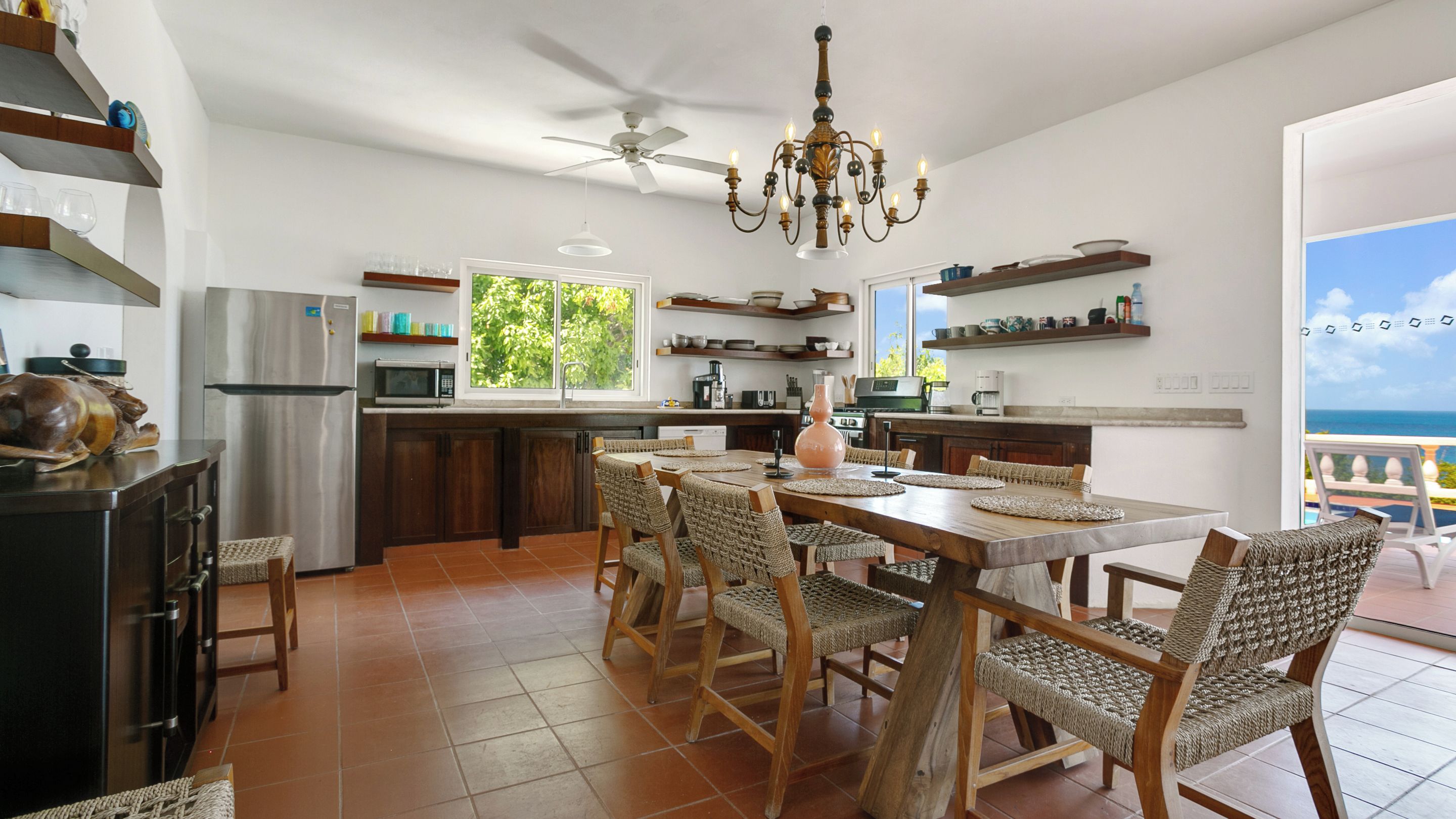 A spacious kitchen with a dining area, a chandelier, and a view of the sea.