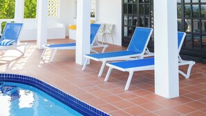 Un edificio de dos pisos con piscina, sillas de descanso azules y un balcón con barandillas negras.