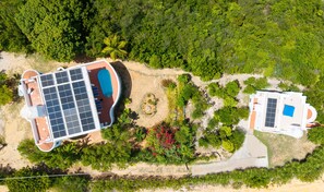 Vista aérea de un complejo turístico con piscina, paneles solares y una zona de playa.