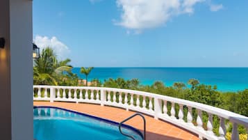 A pool with a white balustrade, a clear blue sky, and a view of the ocean.