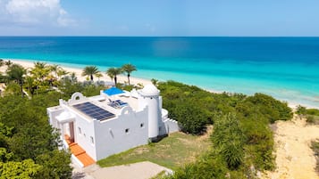 A white building with a solar panel, a beach, and a clear blue ocean.
