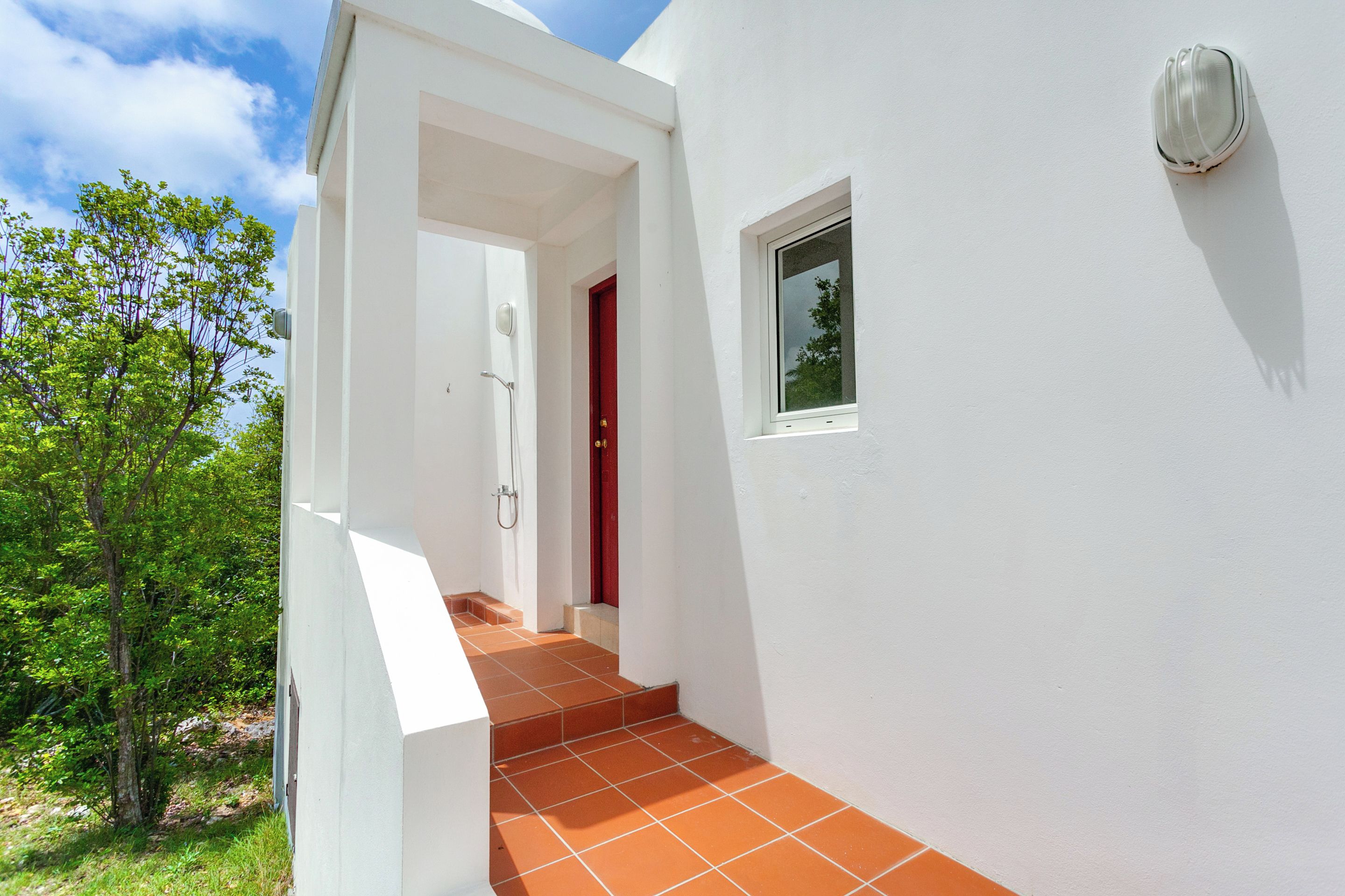 Un bâtiment blanc avec une porte rouge, une petite fenêtre et un porche carrelé.