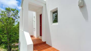 Un bâtiment blanc avec une porte rouge, une petite fenêtre et un porche carrelé.