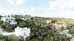 Zona residencial costera con varias casas, algunas con balcones, rodeada de exuberante vegetación y palmeras.