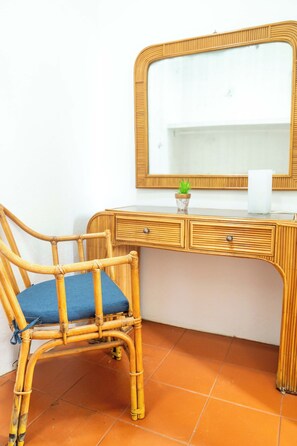 A room with a wooden desk, a chair with a blue cushion, a mirror, and a small potted plant.