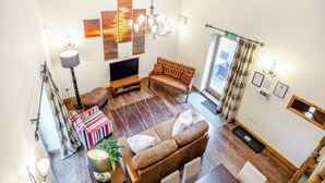 A spacious living room with a large TV, comfortable seating, a chandelier, and a view of the outdoors. - The Granary - UK44520 (Holton-Le-Clay, near Cleethorpes)