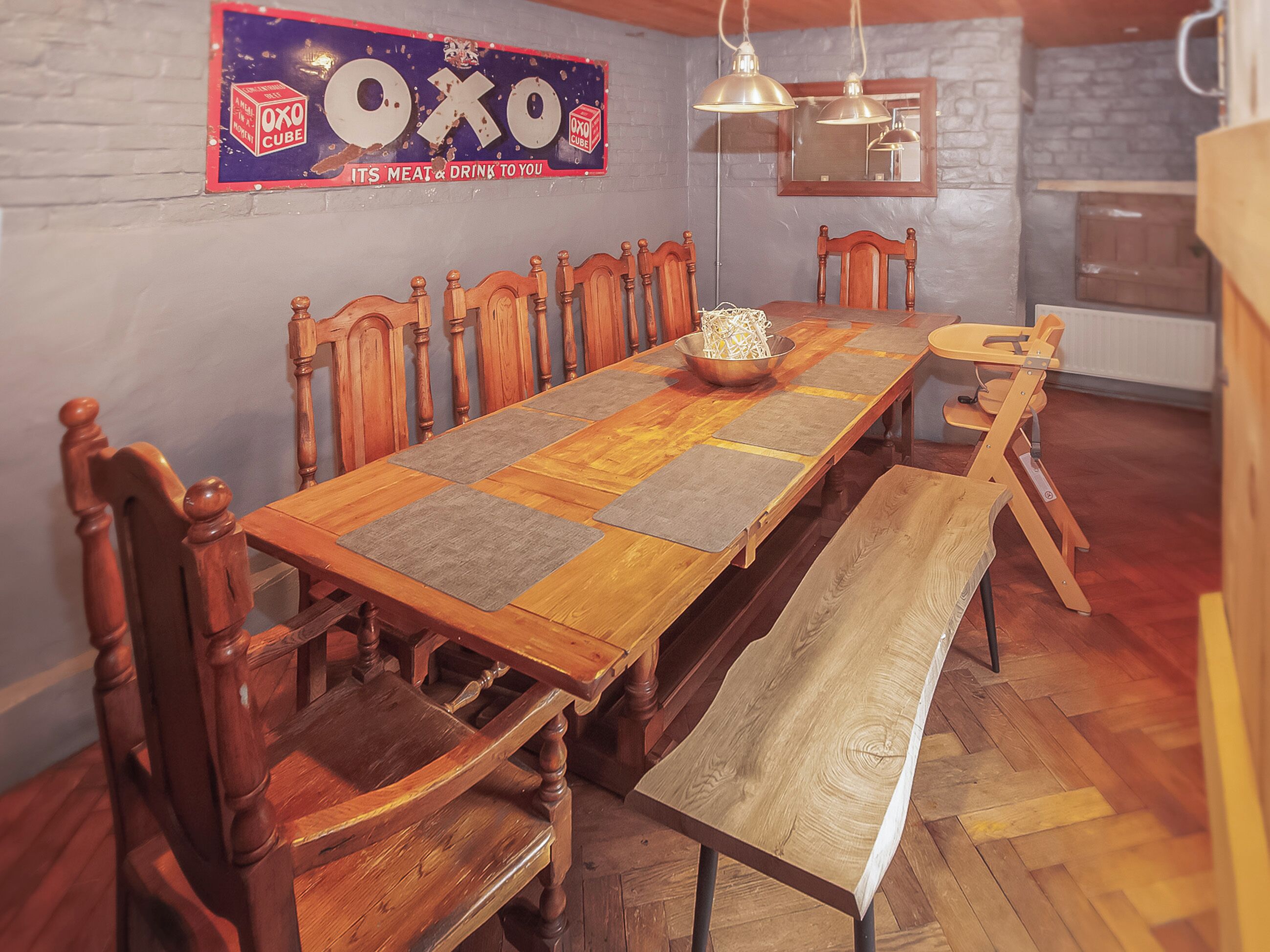Ein Esszimmer mit einem langen Holztisch, Stühlen, einer Bank, einer dekorativen Schale und einem Wandschild.